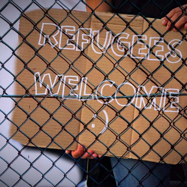 Pappschild hinter einen Drahtzaun mit der Aufschrift "Refugees Welcome"
